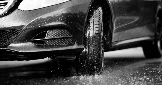 A large stream of spray erupts from under the wheels, flying far around. Black and white color grading. Slow mo, slo mo, slow motion, high speed camera Phantom