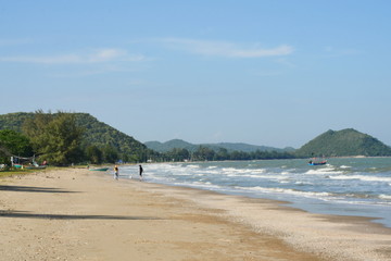 The white wave bubbles in the green water splash the brown sand, Travelers man and a woman and the dog are walking on beach, Sea with  mountain and blue sky at Khao Sam Roi Yot National Park, Thailand