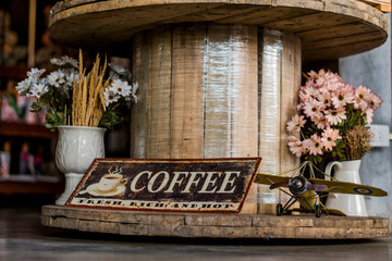 Fototapeta na wymiar Coffee sign, toy helicopter And fake flowers in a vase that is displayed on a wooden table.