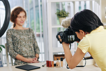 Fototapeta premium Female phoographer taking photo of young woman sitting in beauty studio with fresh make-up