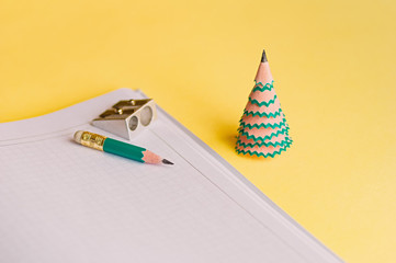 Creative christmas tree. Diary, pencil, shavings and sharpener on a yellow background. Christmas...