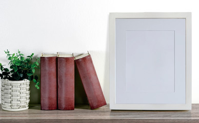Mockup wooden picture frame with books and pencil on wooden table wih old concrete wall.