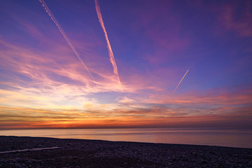 Bewitching gradient sky with plane traces after sunset at sea