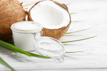 Coconut oil in airtight glass jar and shell pieces on white wooden table