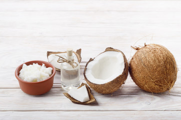 Background of coconut, coconut shell, oil in clay bowl and glass jar on white wooden table