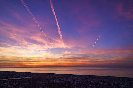 Bewitching gradient sky with plane traces after sunset at sea © Goffkein