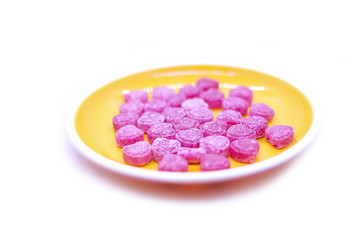 Bright colored candy sweets in a yellow plate on a white background top view