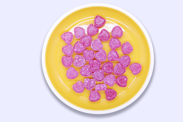 Bright colored candy sweets in a yellow plate on a white background top view