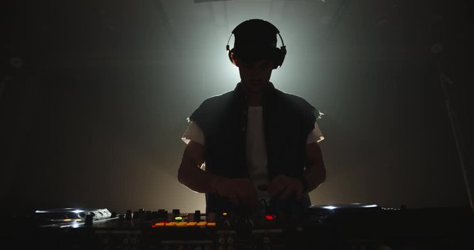 Cool hipster disc jockey performing in a nightclub at a mixer controller, dancing in a dark room - nightlife concept 4k footage