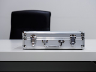 A metal briefcase lying flat on a table in an office setting. Business deal / cash transaction concept