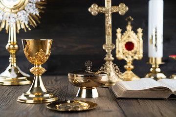 Roman Catholic Church theme. The Cross, Holy Bible, monstrance, rosary and golden chalice on rustic...
