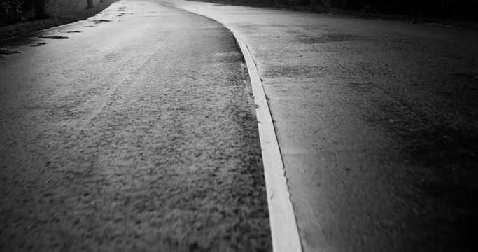 Countryside, wet, single-lane in both sides, asphalt road, separated by a white solid line. Black and white color grading