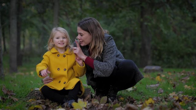 attractive young woman and cute smiling female child are relaxing in the autumn park in the meadow during the fall season, shhh!