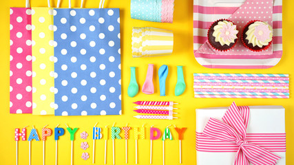 Obraz premium Colorful birthday party flat lay with party food, balloons, decorations and gifts on yellow background.