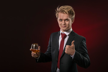 Serious young business man holding a glass of cognac gesturing  perfect by fingers