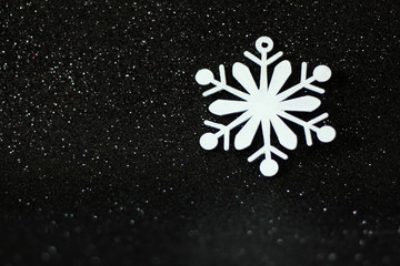Simple Christmas or winter concept: white, decorative snowflake, located on the right side, black glitter background, selective focus, free copy space