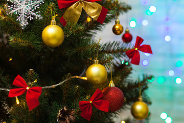 Beautiful green Christmas tree decorated with yellow balls, red bows and garlands. Close-up photo. Sparkling background