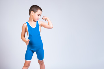 Portrait of a little cheerful boy in a blue  wrestling tights shows biceps, looks confidently at him and poses on a white isolated background. The concept of a little fighter athlete