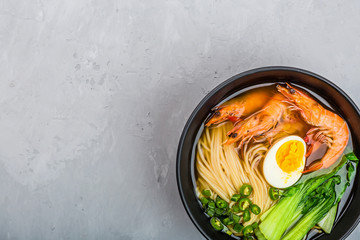 Asian noodle soup, ramen with prawn shrimp, vegetables and egg in black bowl on gray concrete background. Flat lay, Top view, mock up, overhead. Healthy food concept