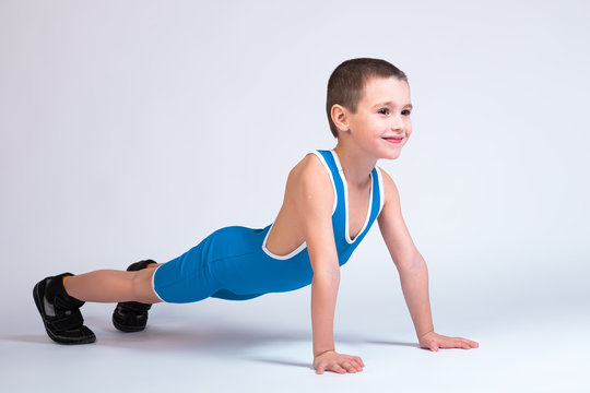 Portrait of a little cheerful boy in a blue wrestling tights and p stands on his hands in a push-up pose, looks forward and poses on a white isolated background.  concept of a little fighter athlet