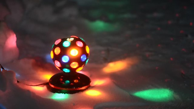 The old Disco ball spinning while standing on the white snow under the Christmas tree casting colorful reflections of the festive night.