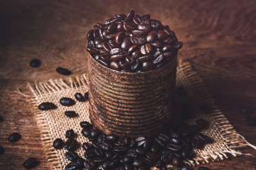 Dark roasted coffee beans in a rusty can on burlap and wood table. Dark mood coffee beans photography.