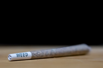 Weed joint on wood, with black background which can be used as copy space. Recreational cannabis legalization. 