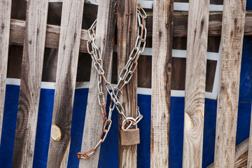 A rusty padlock hanging on a chain on an old wooden fence