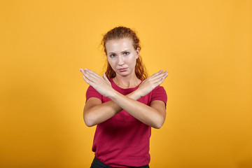Pretty young lady in red shirt doing NO, stop gesture, looking sad isolated on orange background in studio. People sincere emotions, health concept.