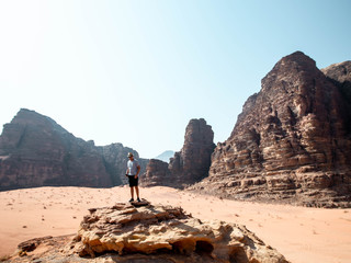 Guy standing on the edge of a cliff in the desert of Wadi Rum with mountains in the background...