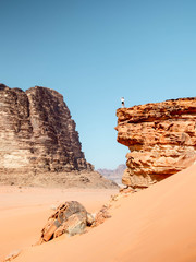 Girl standing on the edge of a cliff in the desert of Wadi Rum viewed from the side of the cliff