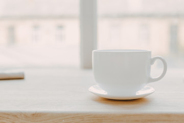 Wooden table with a towel and a white mug on a saucer on a blurred white background of modern kitchen