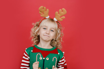 Little girl in Santa elf helper costume on bright red vivid color background.