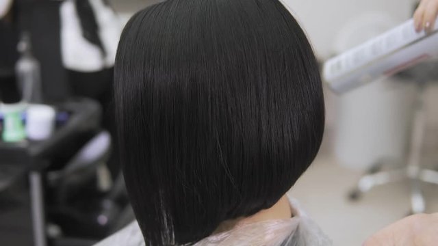 Hairdresser spraying hairspray on hairstyle of beautiful lady in beauty salon. Woman touches hair and uses lacquer to fixate fashion hairdo