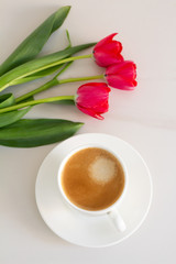 cup of coffee and red tulips on a white background top view