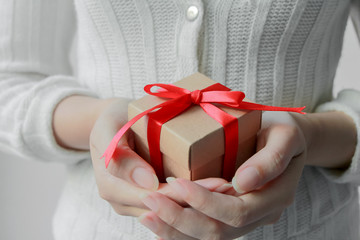 Close up of woman hand holding small brown gift box wrapped with red ribbon.