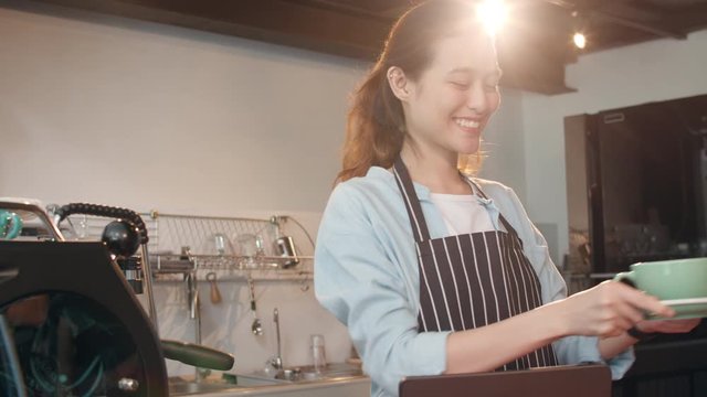 Portrait young Asian lady barista waitress holding coffee cup feeling happy at urban cafe. Asia small business owner girl in apron relax toothy smile looking to camera stand at counter in coffee shop.