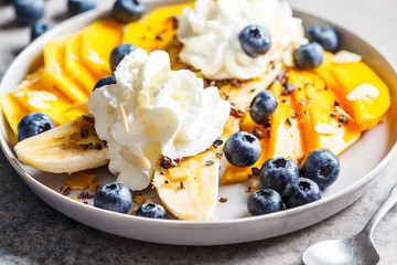 Healthy banana split with mango, chocolate and whipped cream on gray plate.