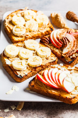 Peanut butter toasts with banana and apple on a gray background.