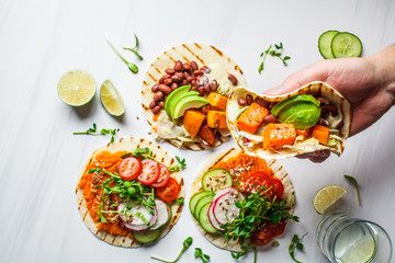 Open vegan tortilla wraps with sweet potato, beans, avocado, tomatoes, pumpkin and  sprouts on white background, flat lay, copy space. Healthy vegan food concept.