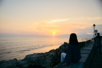 young pretty woman sitting at cliff looking on beautiful sunset