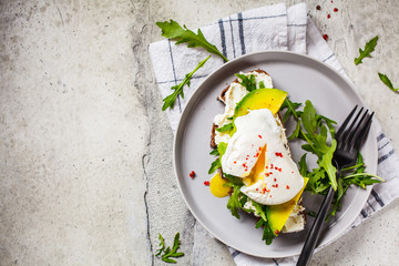 Poached egg toast with avocado, cream cheese and rye bread on gray plate. Healthy food concept.