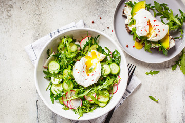 Poached egg toast with avocado, cream cheese and green salad on gray plate. Healthy food concept.