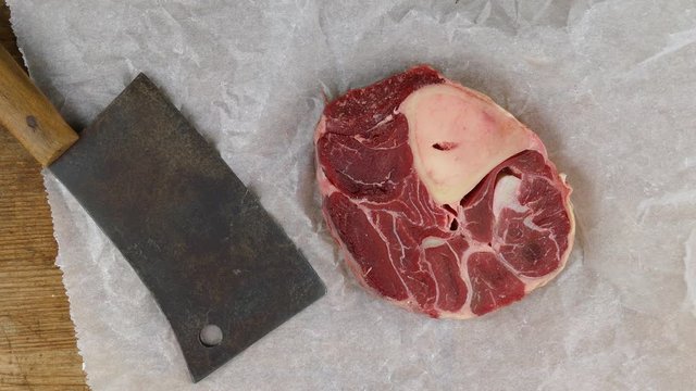 putting a meat cleaver to a fresh beef shank on white wrapping paper on a wooden cutting board top view closeup 4k
