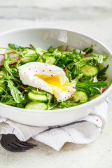 Green salad with poached egg, cucumber and radish in white bowl. Healthy food concept.