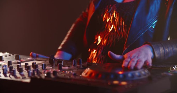 Cool grandmother with authentic outfit and makeup being a funny DJ in a nightclub at mixer controller, rocking the party up 4k footage