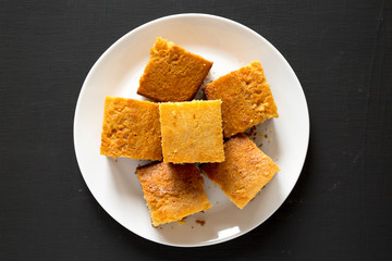Homemade Sliced Cornbread Ready to Eat on a white plate on a black surface, top view. Flat lay, overhead, from above. Close-up.