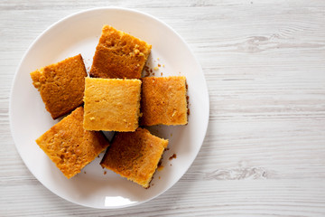 Homemade Sliced Cornbread Ready to Eat on a white plate over white wooden surface, top view. Flat lay, overhead, from above. Copy space.