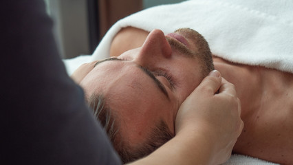 Close up of an young handsome man is receiving a facial massage and spa treatment for perfect skin in a luxury wellness center.