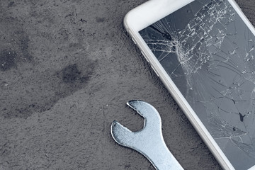 Crashed smartphone with repairing tools on grey background